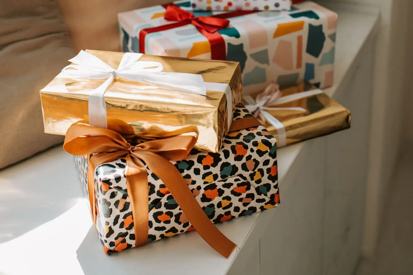 Pila de regalos envueltos en papel dorado, de leopardo y pastel junto a una ventana