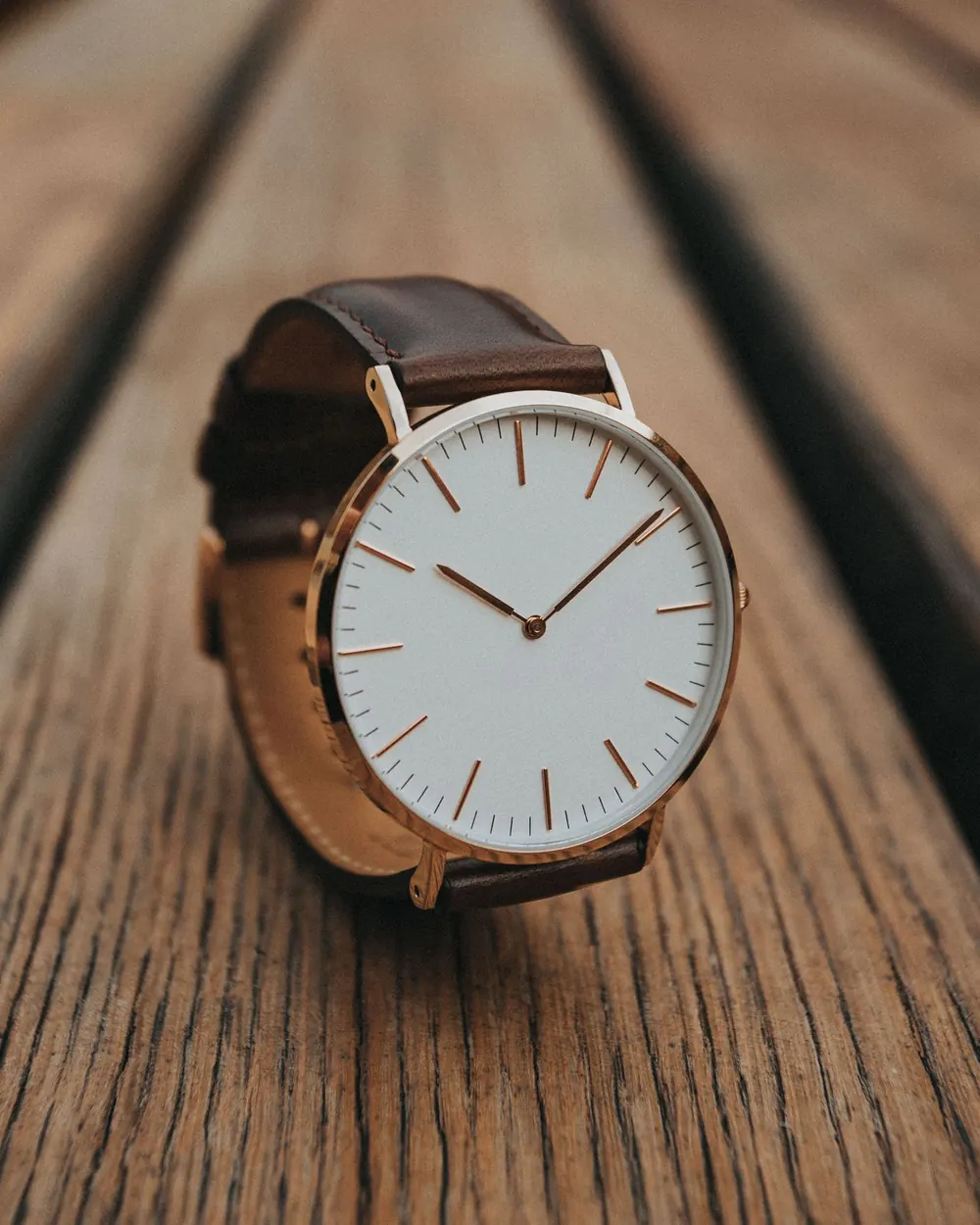 Reloj de caja oro rosa con esfera blanca y correa de cuero café sobre madera