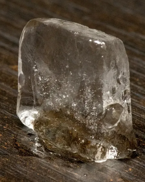 Un cubo de hielo cristalino apoyado sobre madera