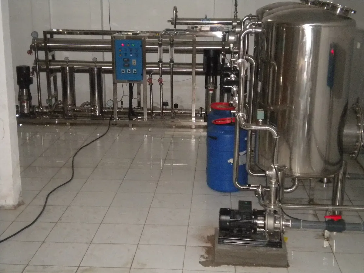 Sistema de filtración de agua con tanque de acero y tuberías sobre piso de baldosa